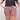 A person wearing faded dusty rose denim shorts with a floral lining visible in the pockets, holding the sides of the pockets outward. The person is also wearing a black t-shirt against a light gray studio background.