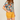 Person wearing a colorful floral shirt and mustard yellow shorts on a plain background