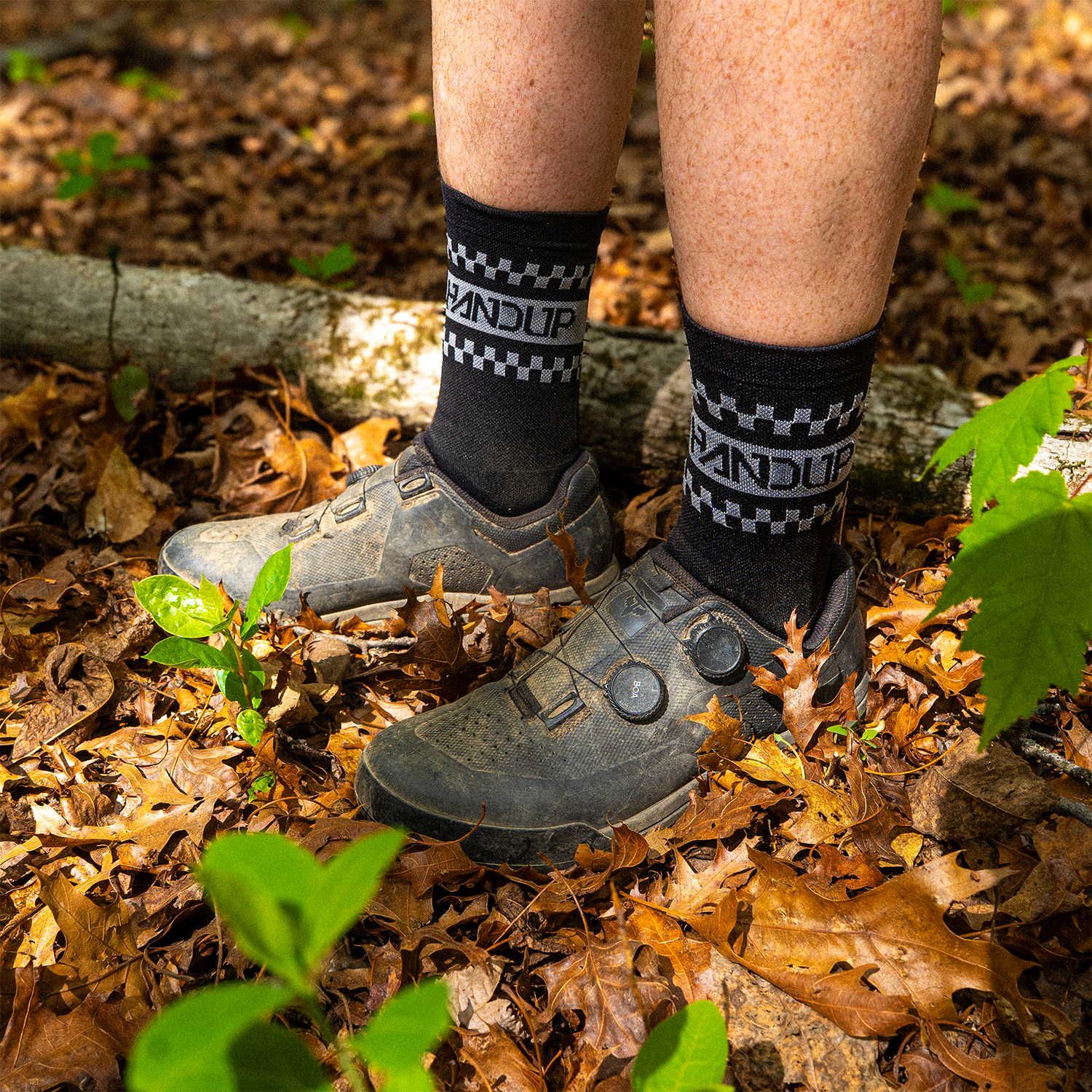 Person wearing black socks with white text and hiking boots on a forest floor.