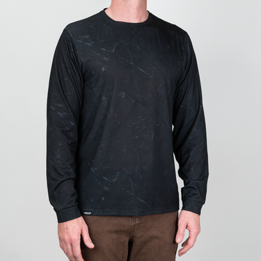 A man wearing a black long-sleeve crewneck shirt with a subtle gray marble pattern, paired with brown pants, against a light gray background.