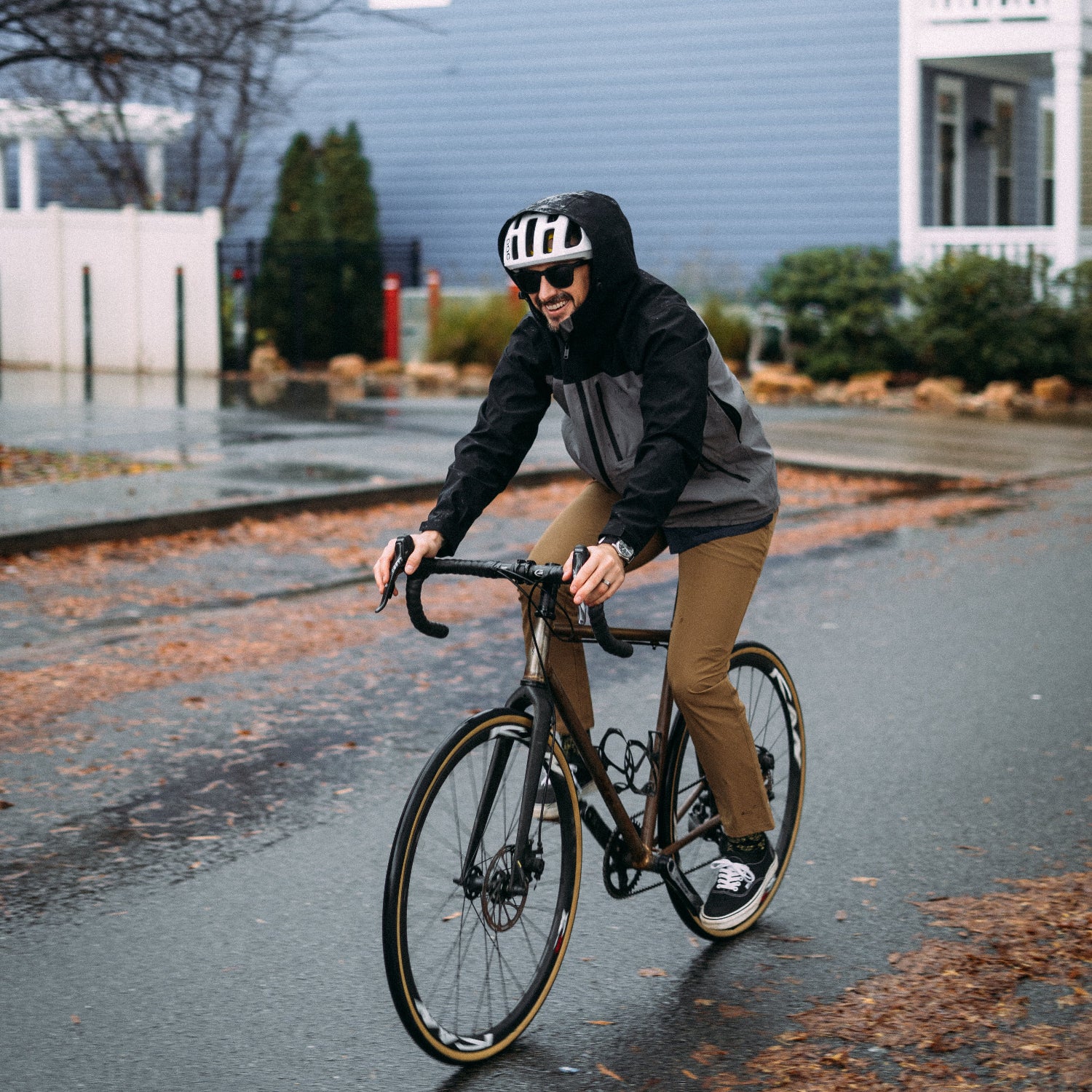 Person riding a bicycle on a residential street with a blue house in the background