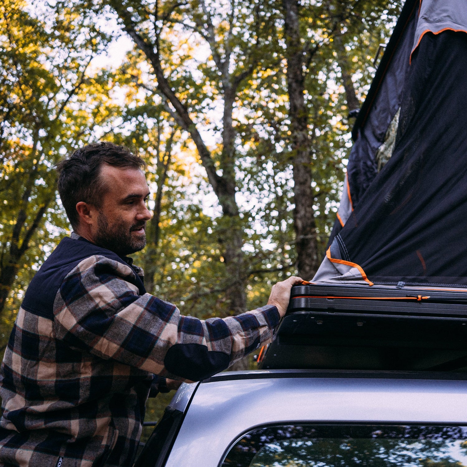 Man attaching a rooftop tent to a vehicle in a forest setting