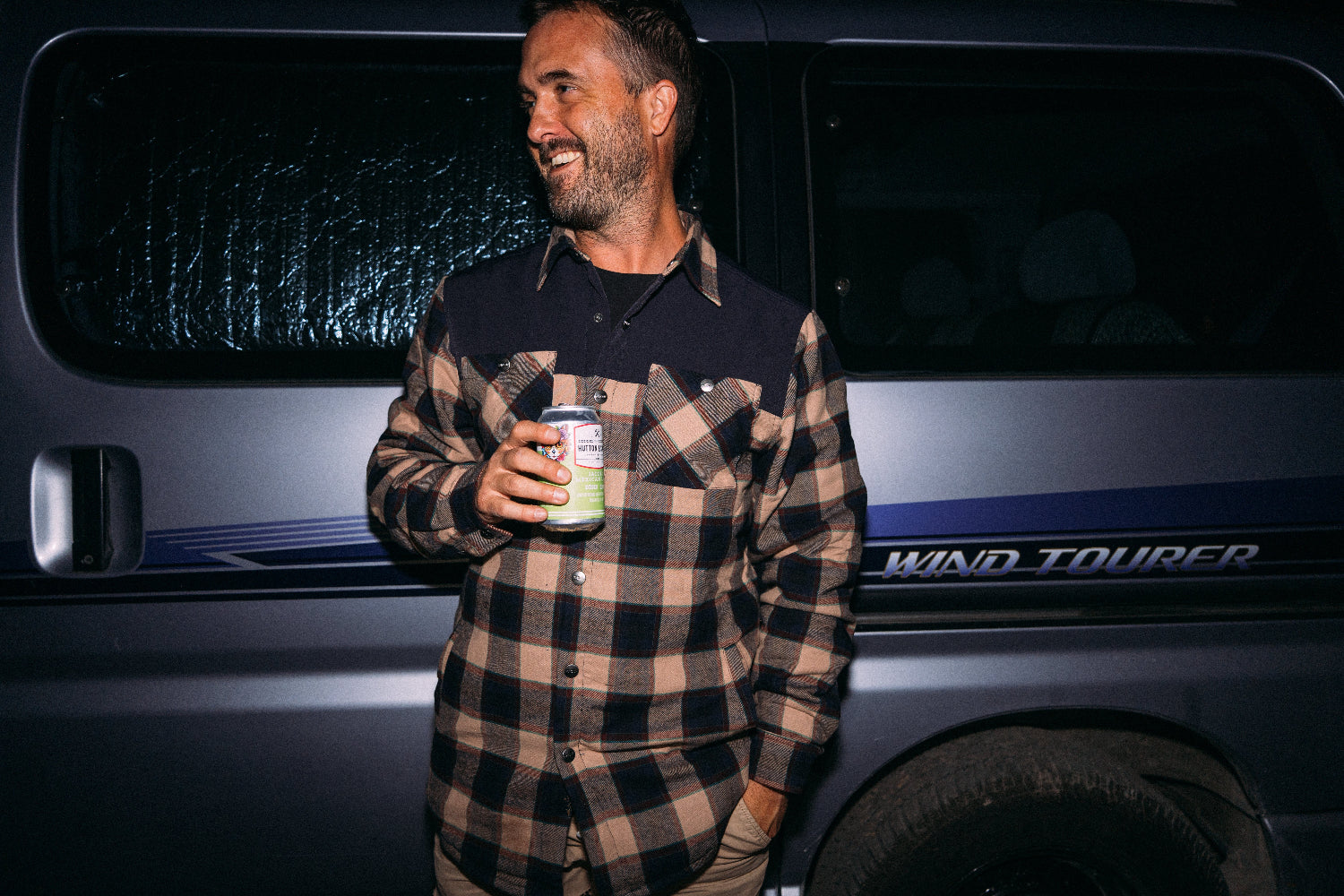 Man holding a can in front of a vehicle with 'Wind Tourer' branding
