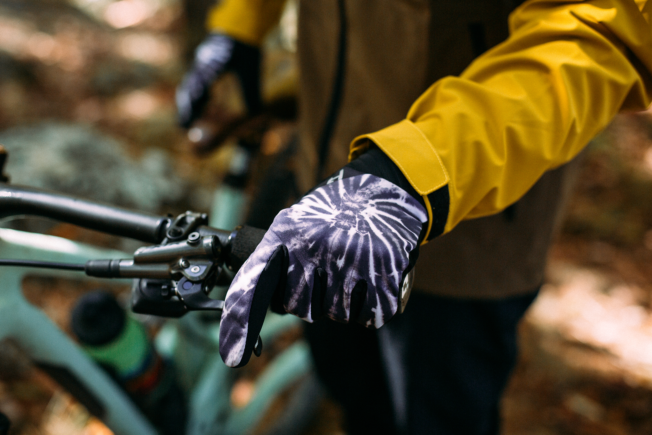 Person wearing a yellow jacket and purple gloves on a bike in a forest