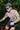Man riding a mountain bike through a forest with another cyclist in the background.