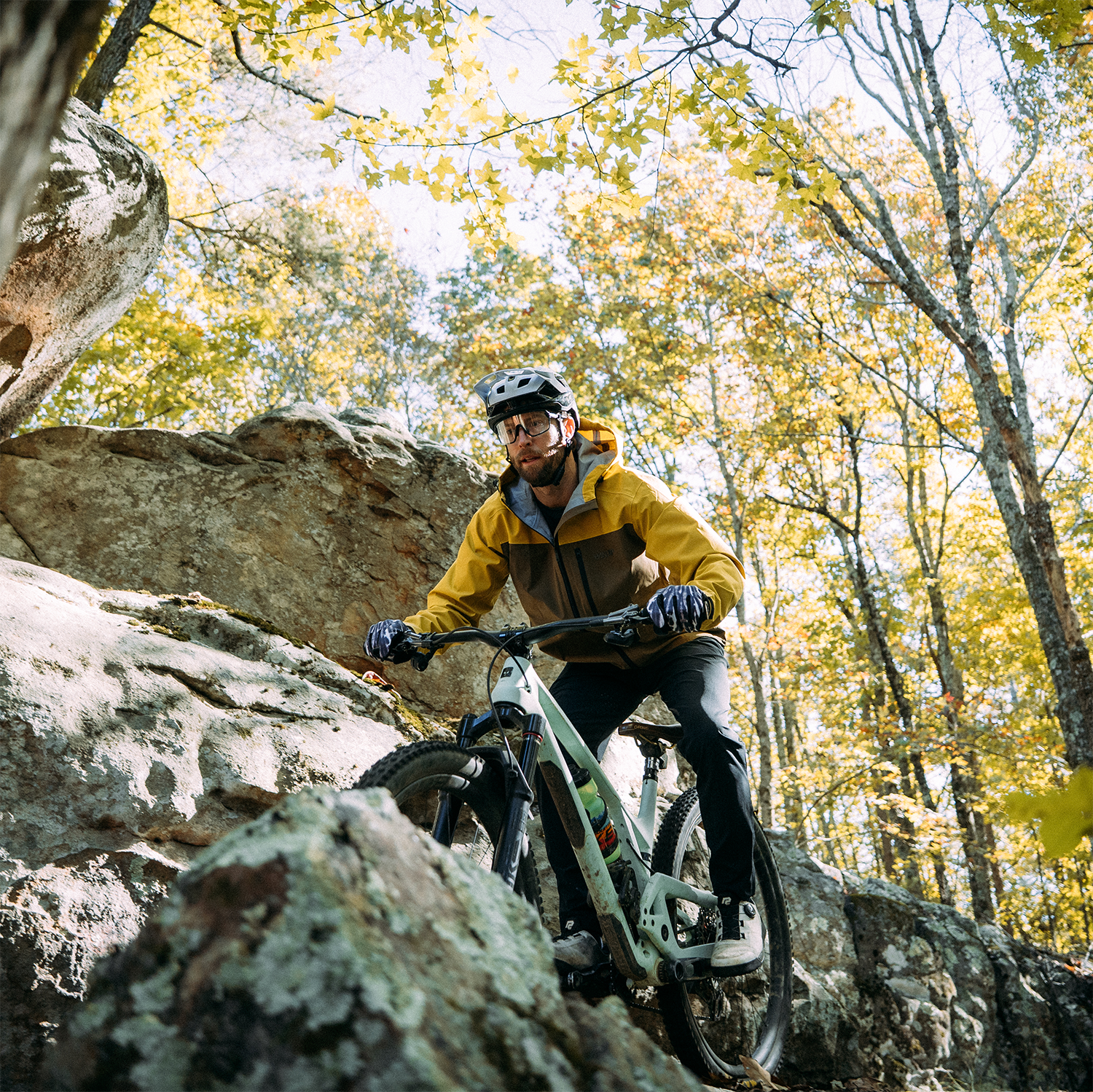 Man riding a mountain bike on rocky terrain with autumn trees in the background