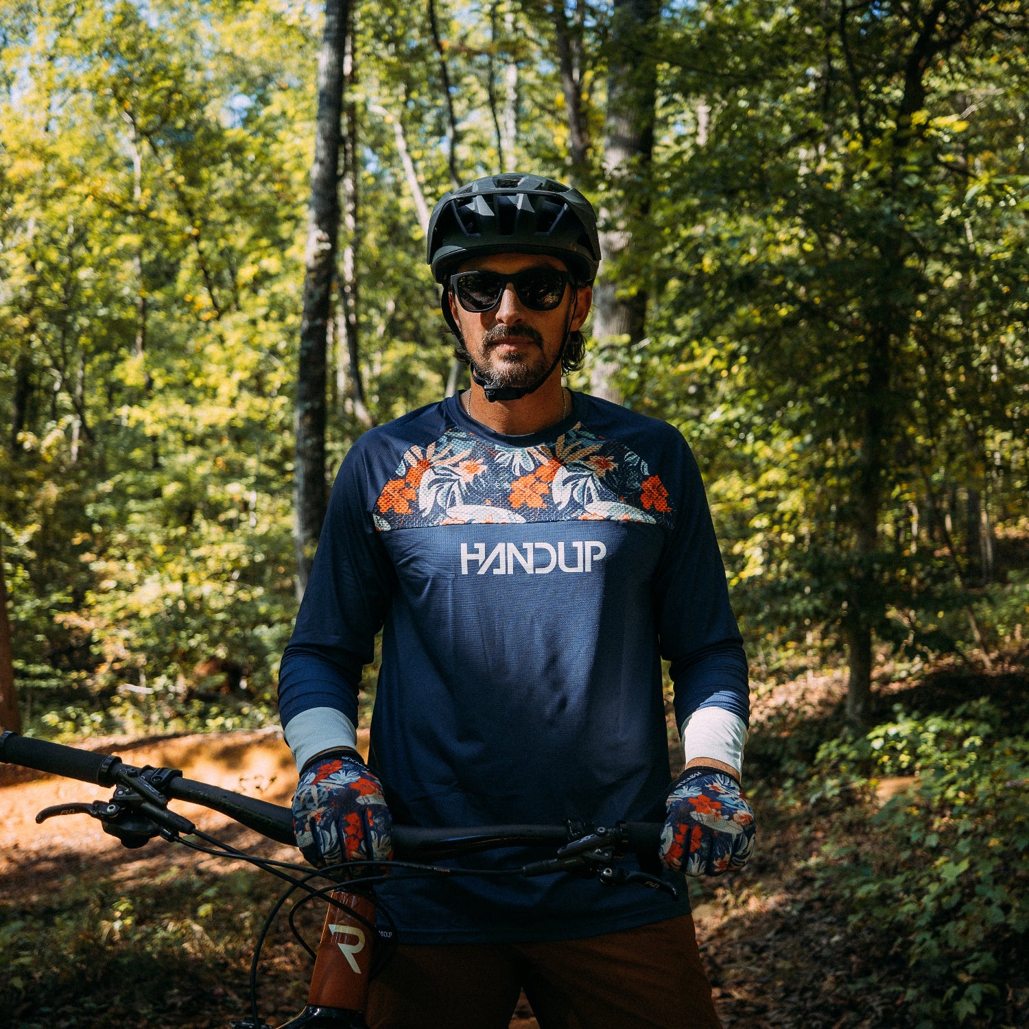 Man in a forest wearing a helmet and 'Handup' shirt holding a bike
