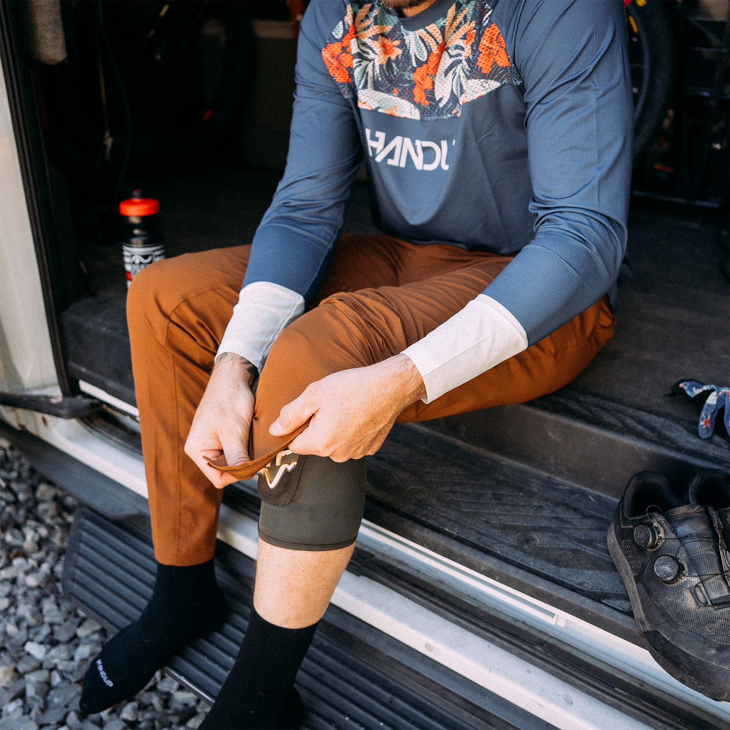 Person sitting in a vehicle wearing a blue long-sleeve shirt with floral design and brown pants.
