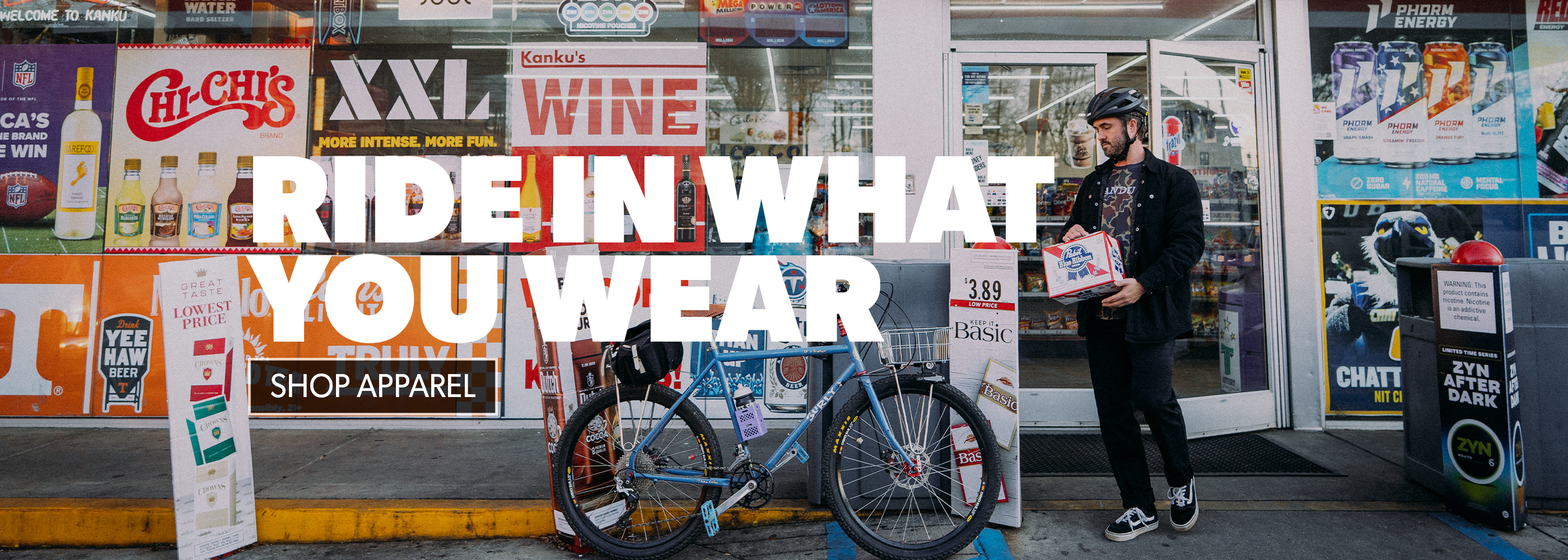 Person with a bicycle and shopping bags in front of a store with promotional signs.