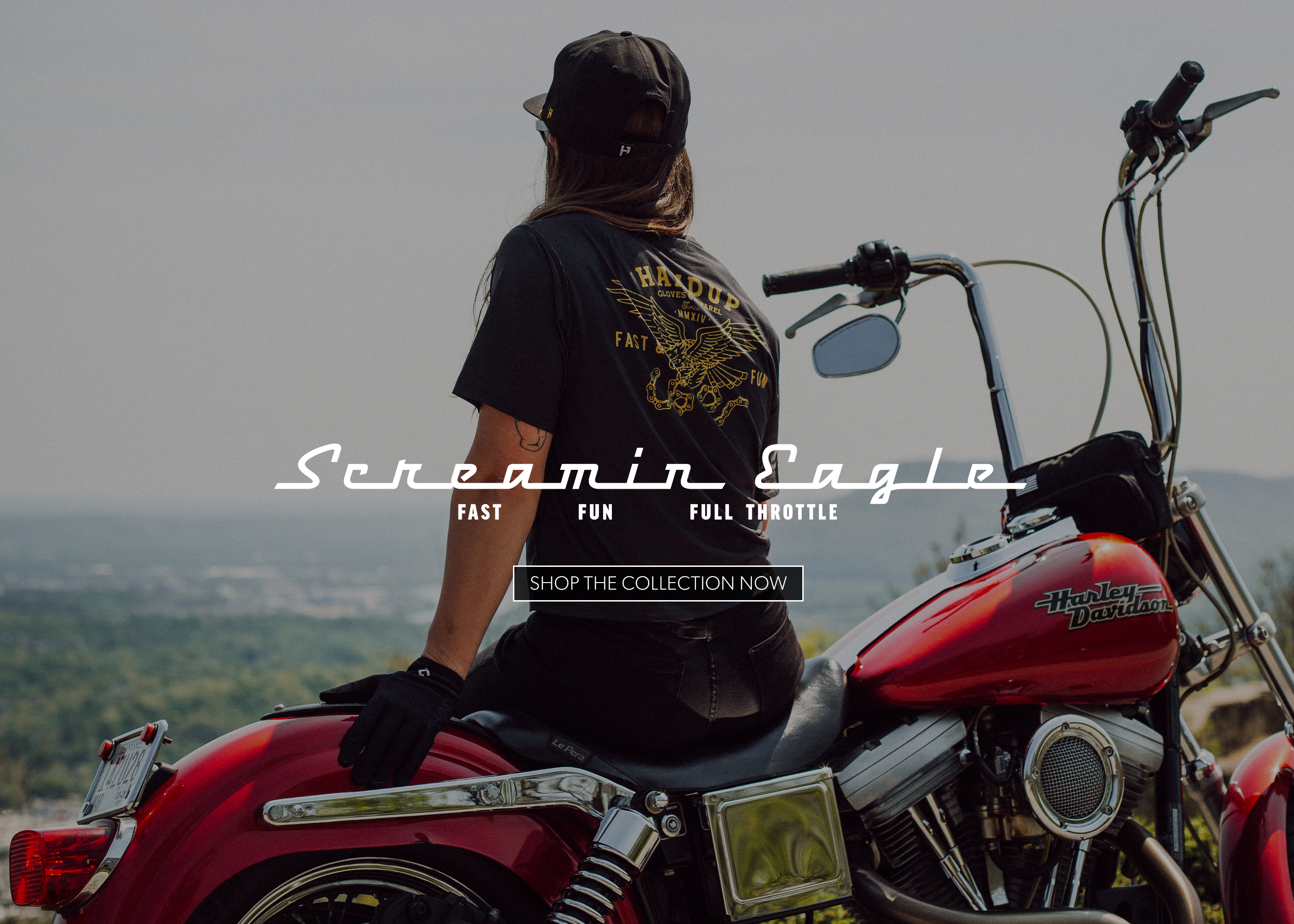 A person wearing a black graphic t-shirt and cap sits on a red Harley-Davidson chopper motorcycle, viewed from behind. The image has a scenic, hazy background and features a text overlay that reads 'Screamin Eagle' and 'SHOP THE COLLECTION NOW'.
