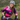 A woman smiling while riding a mountain bike in an outdoor grassy, hilly environment. She is wearing a white helmet, a pink and purple gradient cycling jersey with 'TRIPLE T' and 'HACCO' logos, black cycling shorts, and colorful gloves.