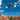 A mountain biker mid-air performing a jump over a desert canyon with red rock formations and blue sky with white clouds.