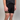 Person wearing black shorts with a brand logo on a plain background