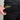 Person wearing black pants with a visible brand logo, holding a phone case with a pattern.