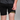 Person wearing black shorts with a yellow band around the waistband against a gray background