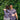 Two people in floral shirts embracing in front of a green leafy background