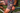 Close-up of a person wearing colorful geometric patterned cycling shorts while sitting on a bicycle outdoors. The shorts feature a busy abstract print in pink, yellow, blue, and black, with a matching compression-style thigh band.