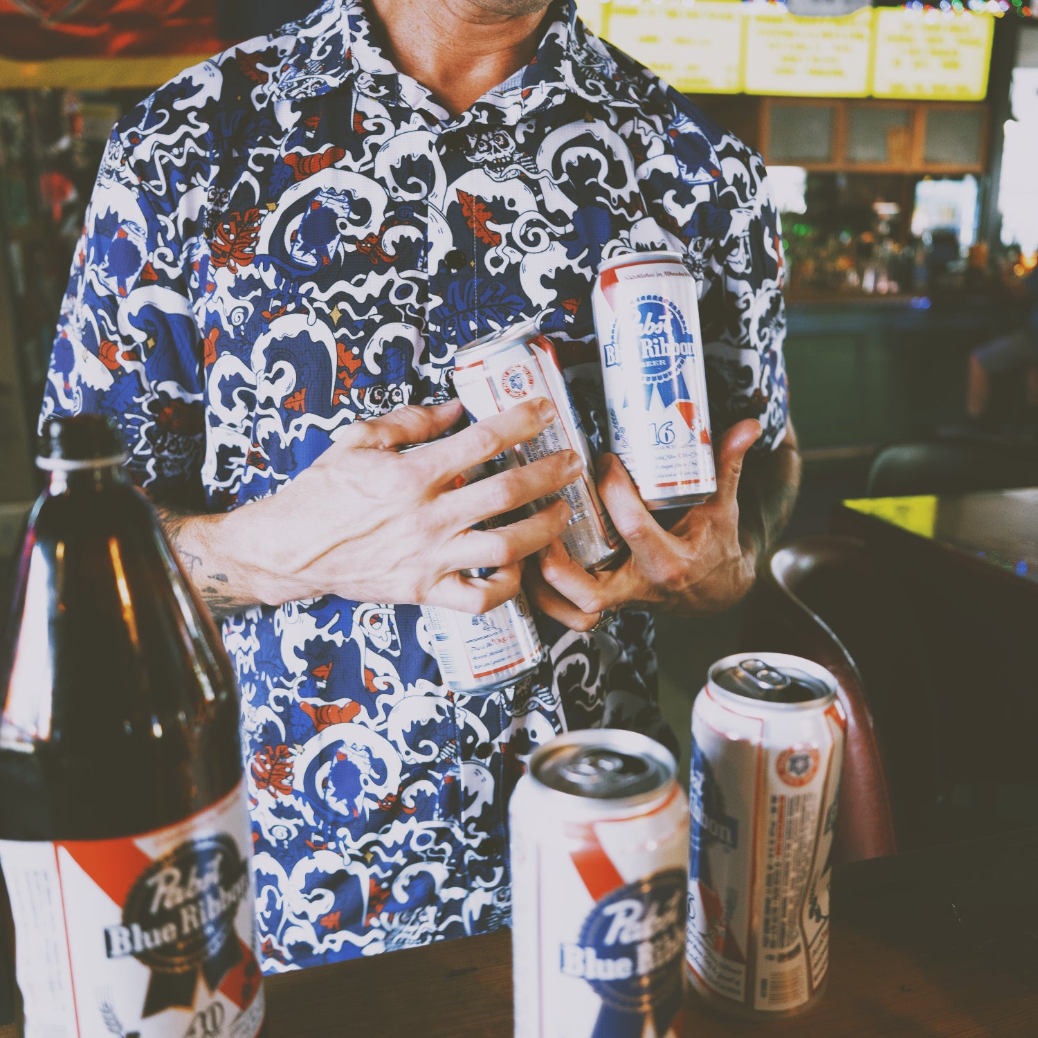 Person holding multiple beer cans in a bar setting