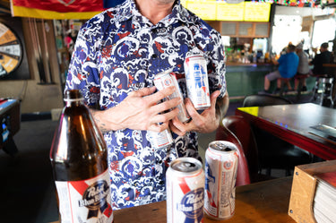 Person holding multiple beer cans in a bar setting