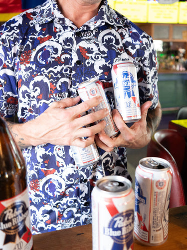 Person holding multiple beer cans in a bar setting