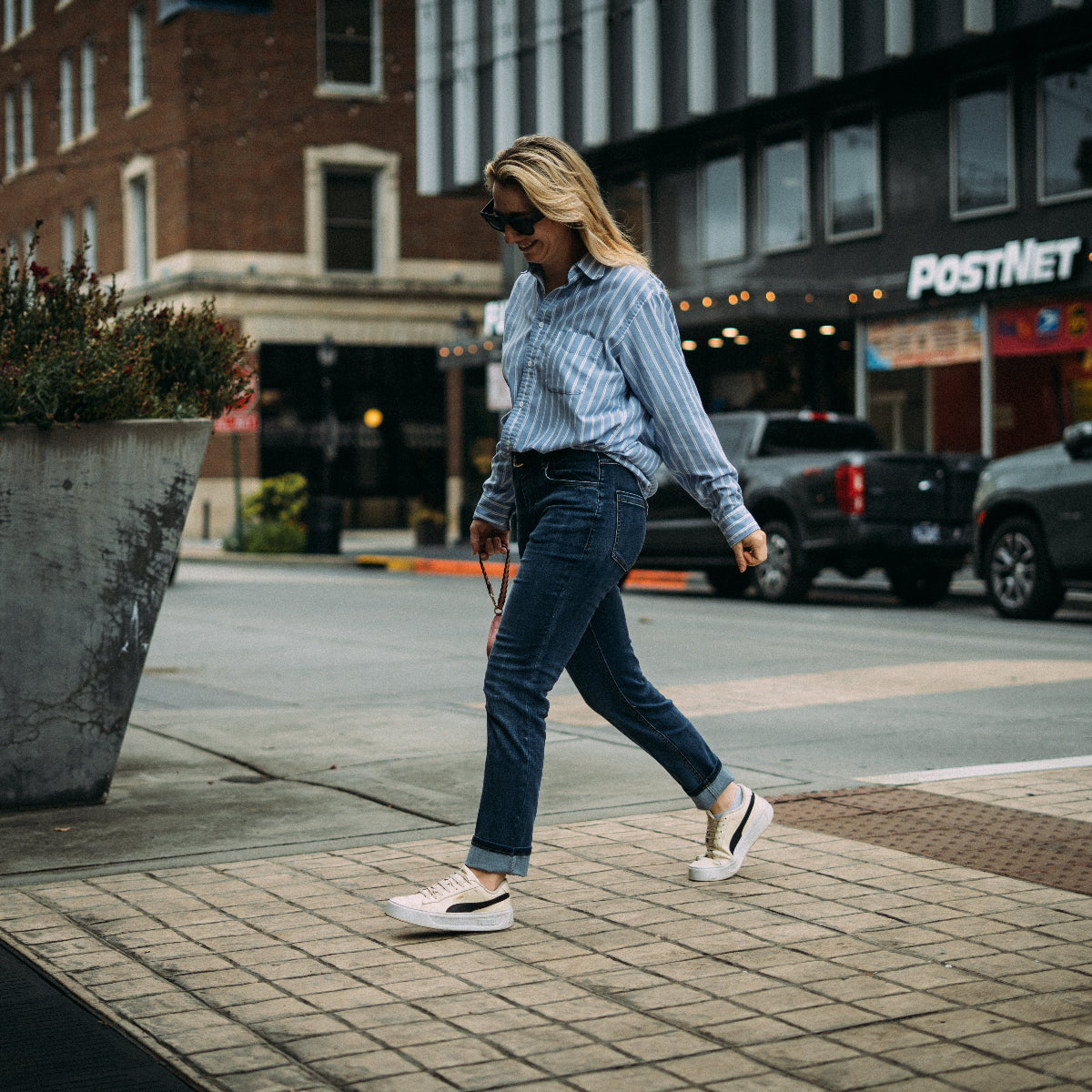 Woman walking on a city street wearing a blue plaid shirt and jeans.