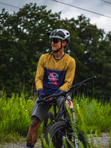 Man with a bicycle on a gravel path surrounded by greenery