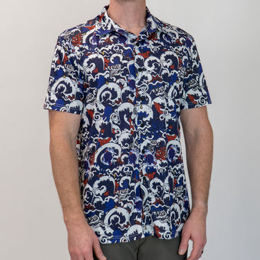 Person wearing a patterned shirt with blue, white, and red design on a plain background