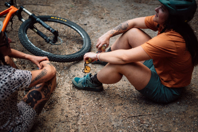 Two people sitting on the ground with a bicycle, one person is adjusting a shoe.