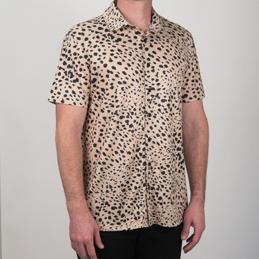 Person wearing a short-sleeve shirt with a cheetah print pattern on a plain background