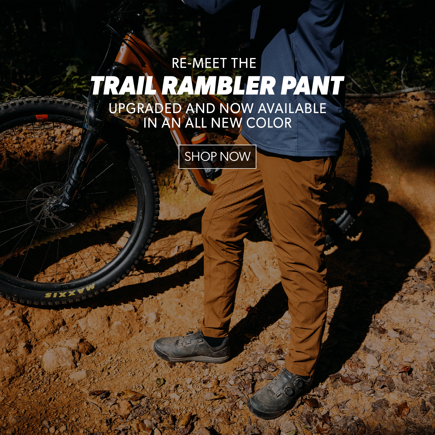 Person wearing brown trail rambler pants standing next to a bicycle on a dirt path.