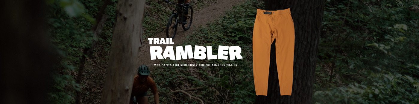 Orange pants displayed with 'Trail Rambler' branding in a forest setting.