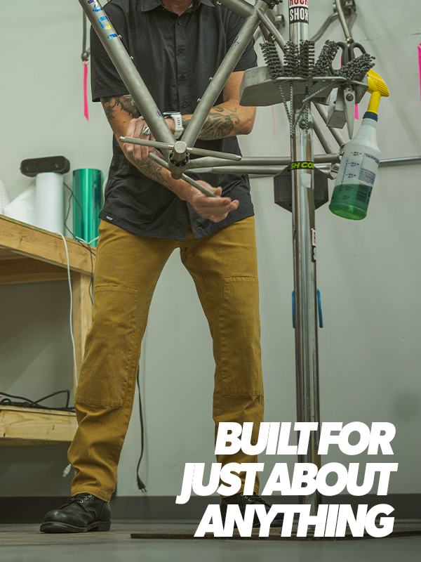 Person working on a bicycle frame with tools and parts in a workshop, text 'Built for just about anything' displayed.