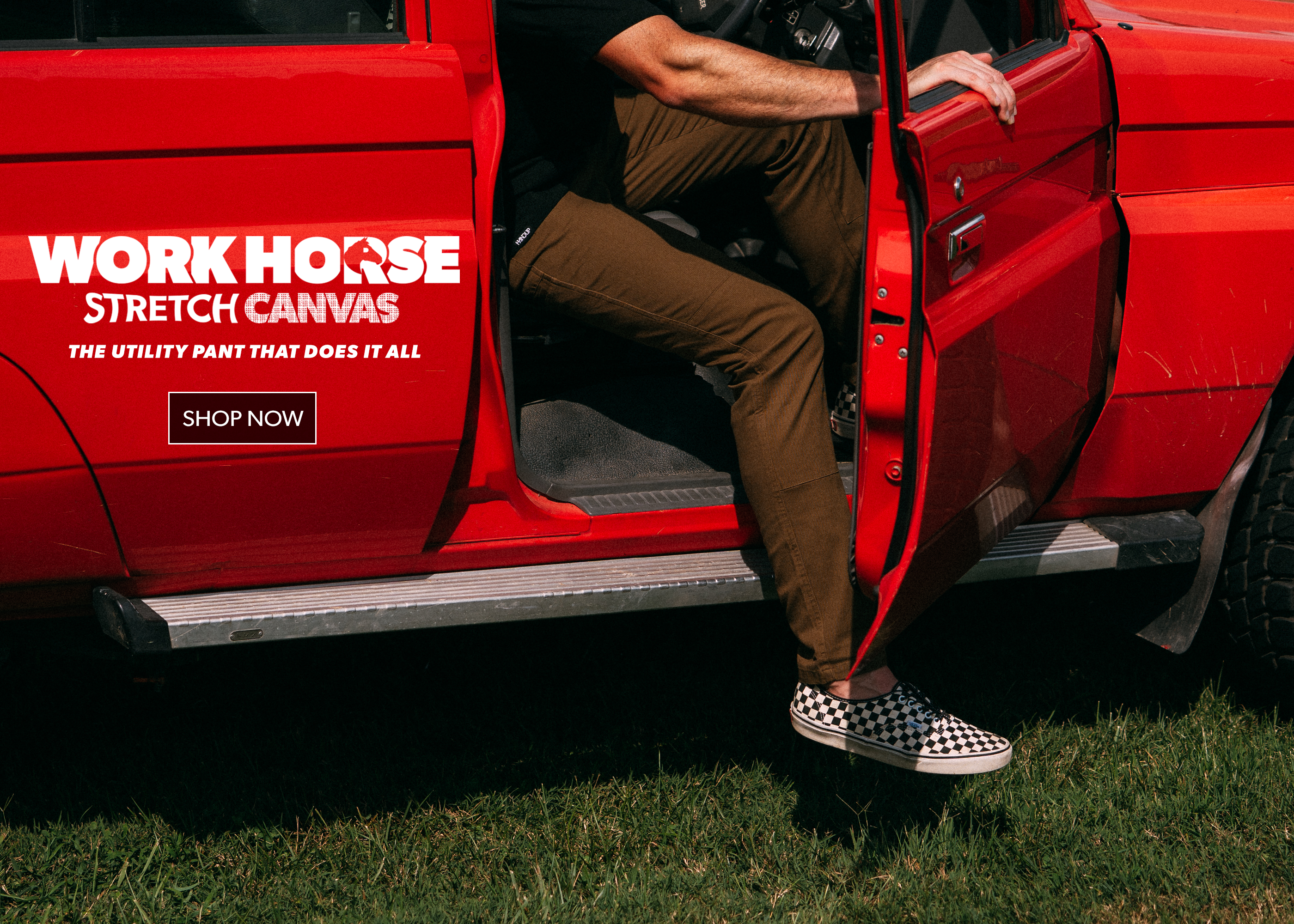 A person wearing brown utility pants and black-and-white checkered slip-on shoes steps out of a red pickup truck. The side of the truck has a large white and red graphic that reads 'WORK HOUSE STRETCH CANVAS' with smaller text 'THE UTILITY PANT THAT DOES IT ALL' and a 'SHOP NOW' box.