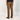 A person shown from the back wearing brown straight-leg pants, a black t-shirt, and black Vans slip-on shoes against a light gray studio background.