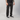 A person wearing black jeans with a subtle dark gray marble or distressed pattern, styled with a black t-shirt and black low-top sneakers with white laces, standing against a light gray studio background.