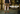 A person standing in a warehouse with stacked wooden barrels, wearing brown canvas work shorts, a black t-shirt, gray socks, and brown leather work boots. Large text on the right reads 'WORK HORSE STRETCH CANVAS' with a 'SHOP NOW' button below.