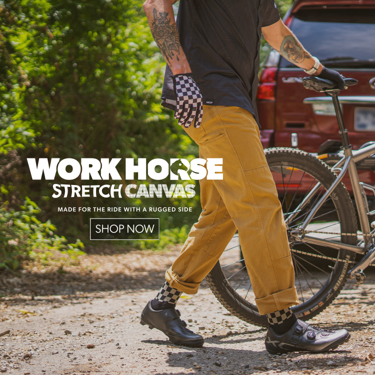 Person in checkered gloves and tan pants holding a bike up with promotion text for Workhorse Stretch Canvas pants