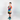 A young boy stands against a light gray studio background wearing a vibrant tie-dye t-shirt with a spiral pattern in blue, yellow, orange, and red, featuring the brand name 'KANDOR' on the chest. He is also wearing black shorts and teal sneakers.