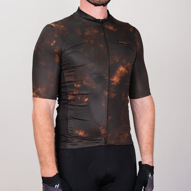 Person wearing a black and orange patterned cycling jersey on a gray background
