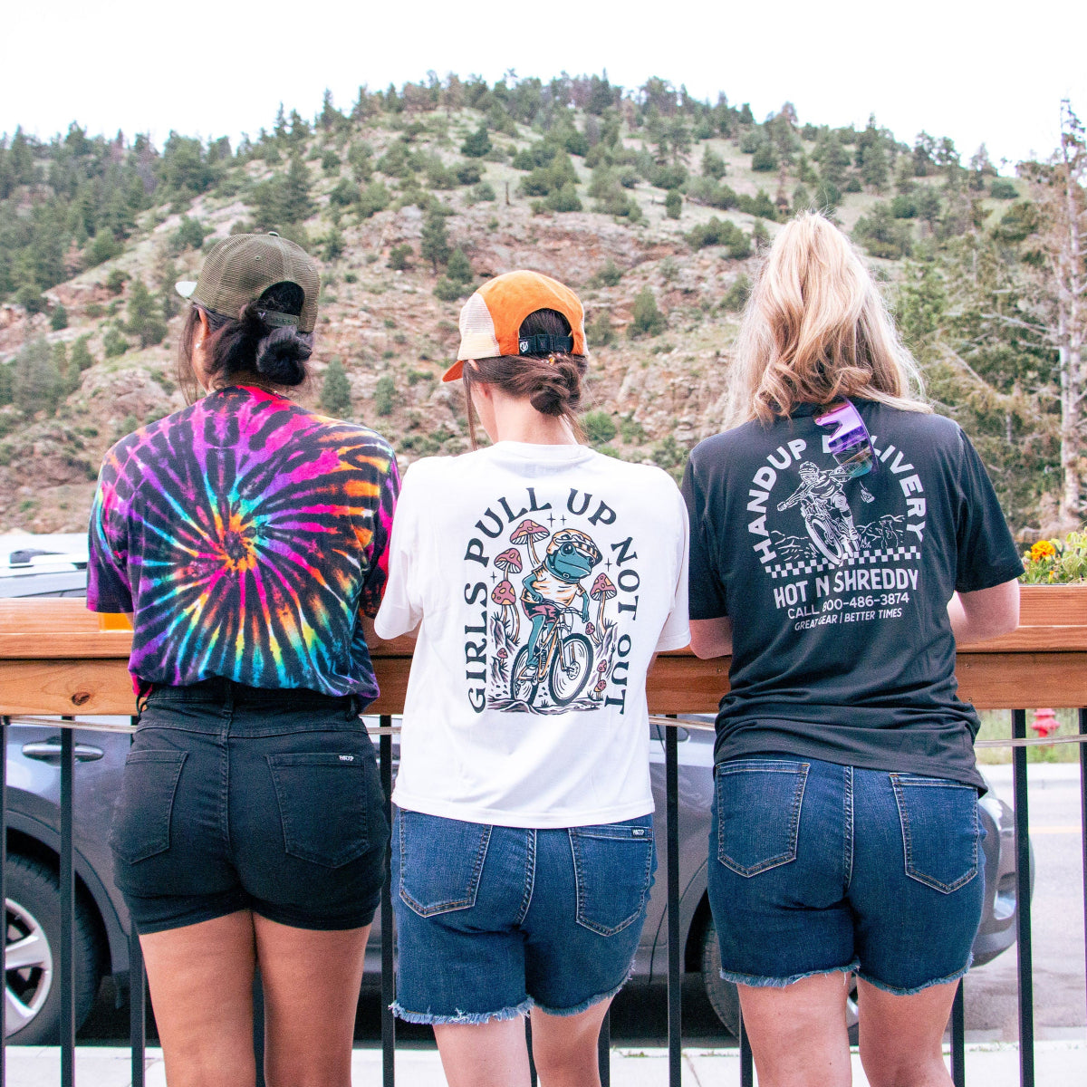Three people standing on a wooden deck overlooking a scenic mountain landscape.