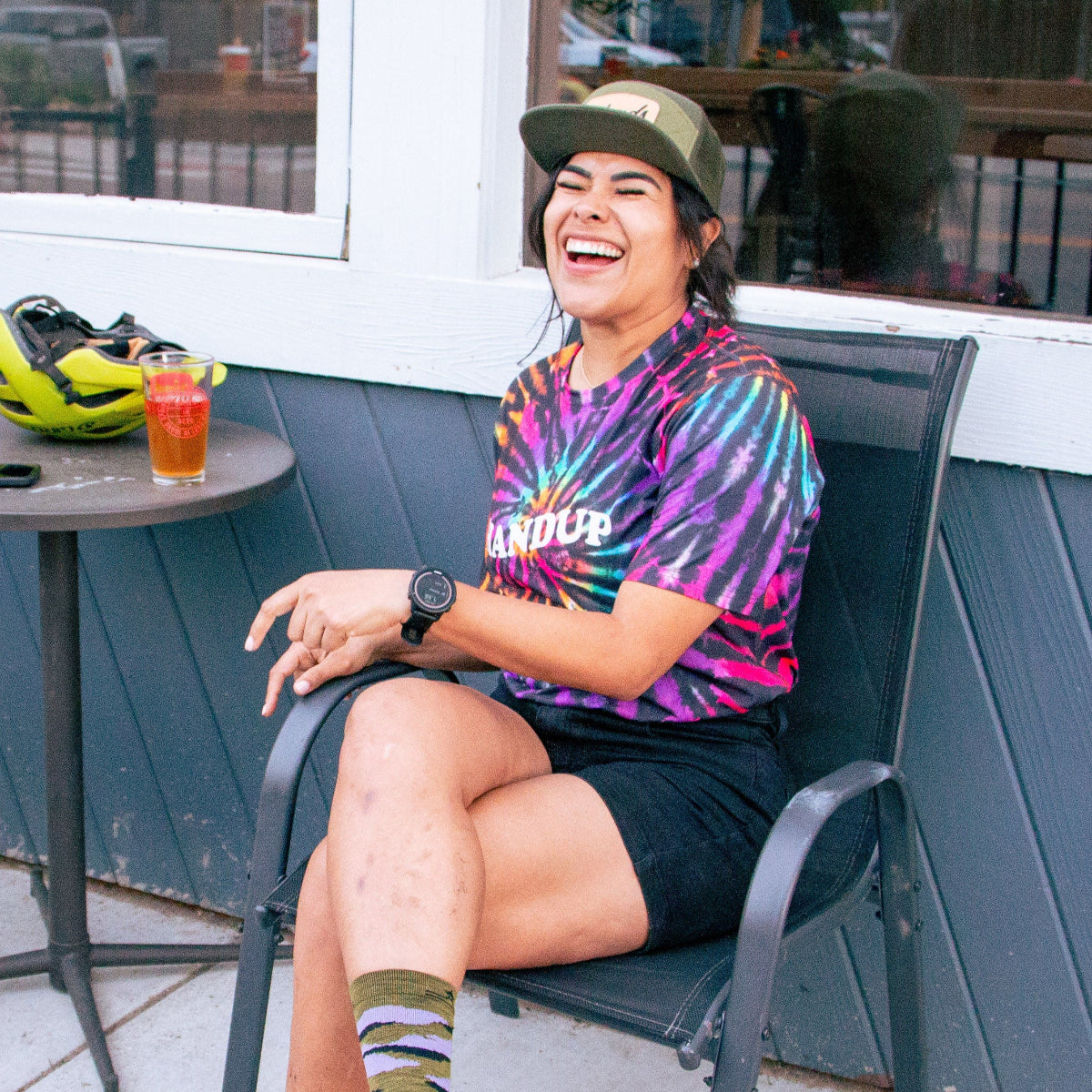 Person sitting on a chair outdoors, wearing a tie-dye shirt and colorful socks.