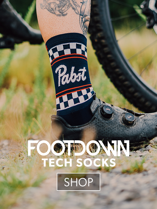 Person wearing a Pabst branded sock with a bike in the background, promoting Footdown Tech Socks.