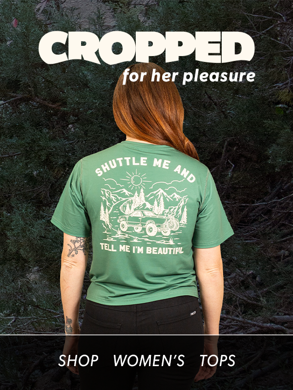 Person wearing a green t-shirt with a graphic design and text, standing against a dark background.